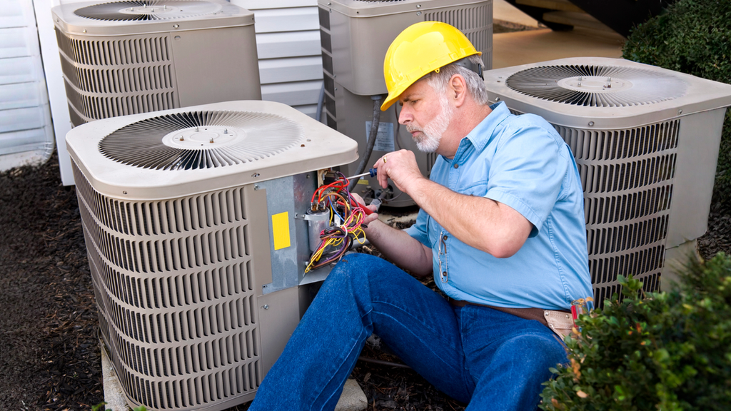 HVAC technician repairing outdoor AC unit during emergency service for urgent cooling system warning signs.