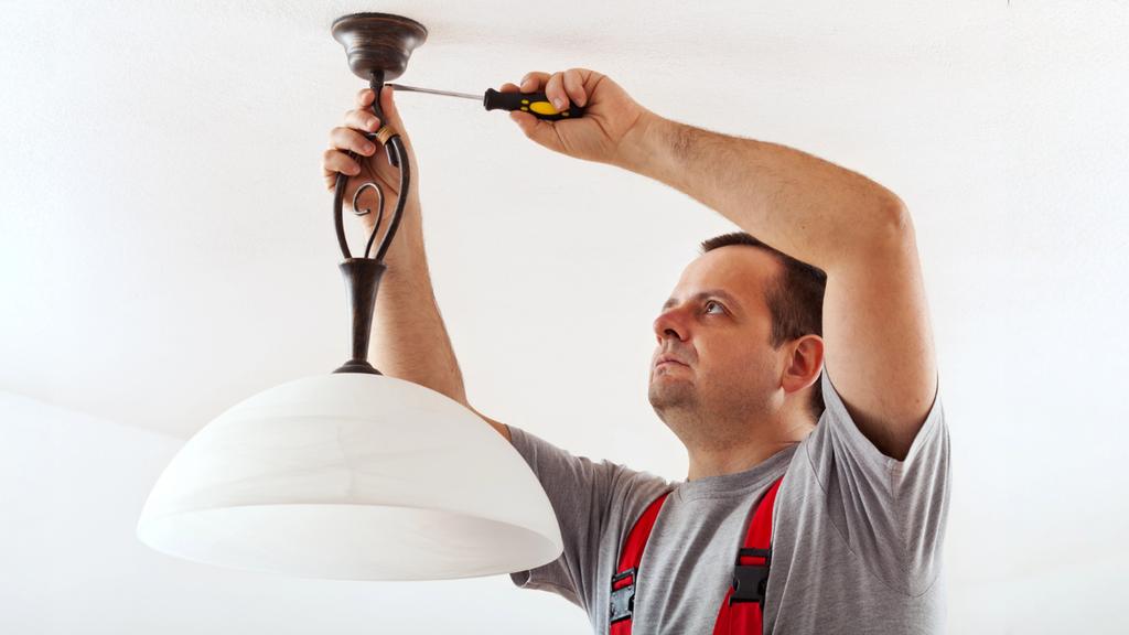 Electrician repairing ceiling light highlights electrical red flags landlords should never ignore in rental properties.