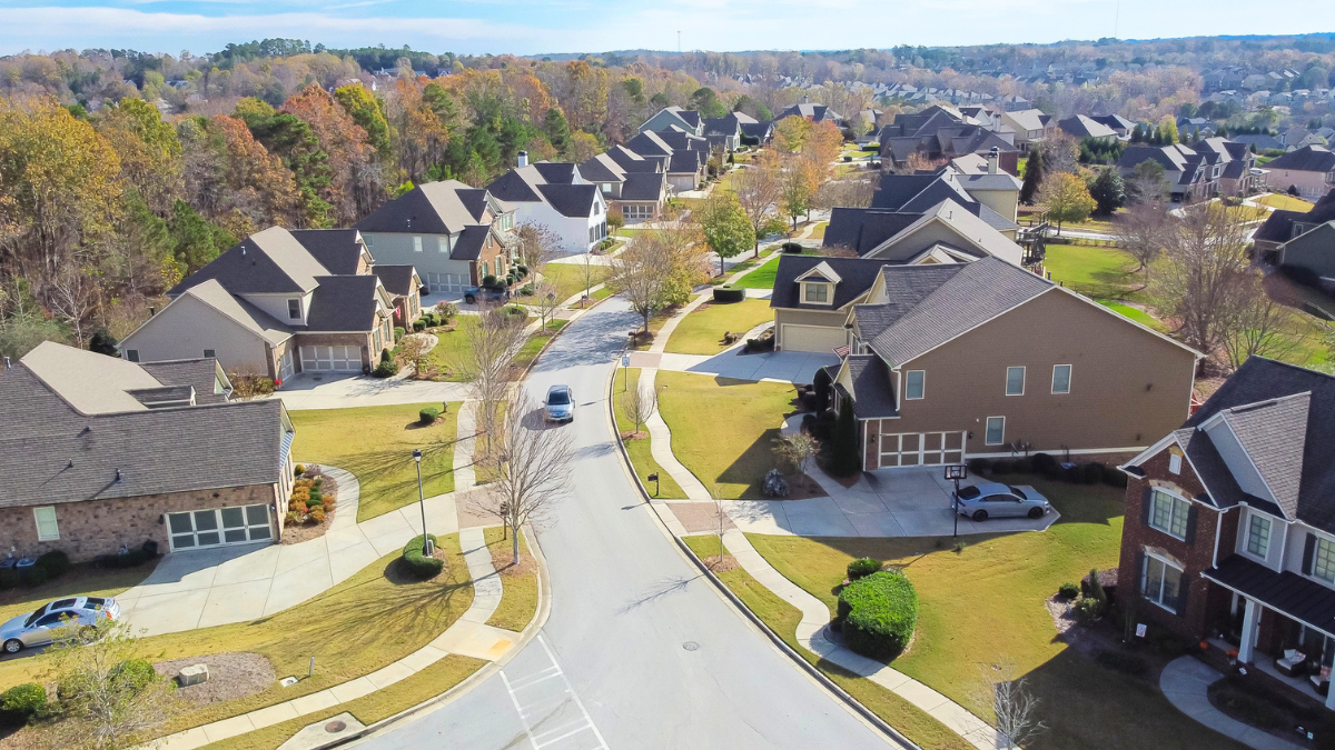 Aerial view of suburban HOA neighborhood with tidy homes, lawns, sidewalks, and streets.