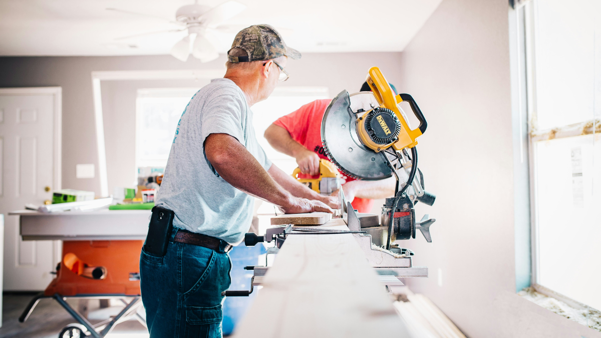 Contractors remodeling home interior with miter saw to increase real estate value through strategic upgrades.