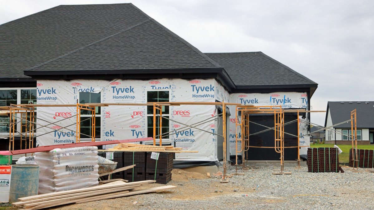 Property owners comparing contractor quotes for home construction project with scaffolding, materials, and exterior work.
