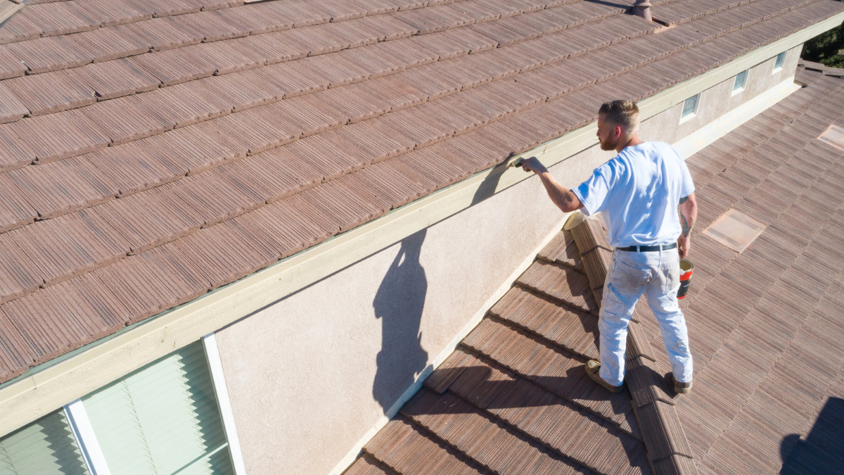 Professional painter on roof painting house exterior.