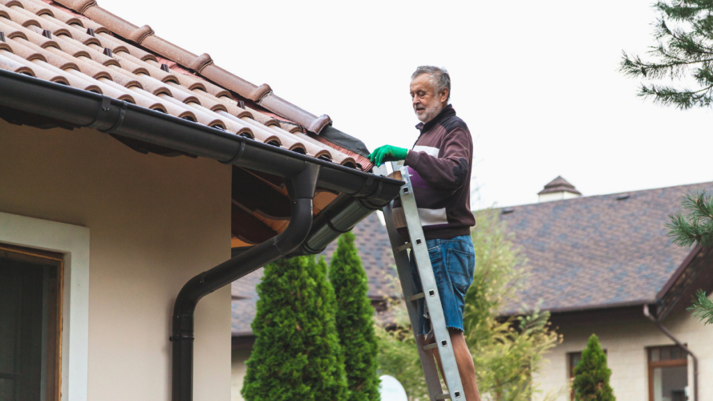Landlord inspecting rental property roof gutters from ladder to prevent damage and maintain roofing asset.