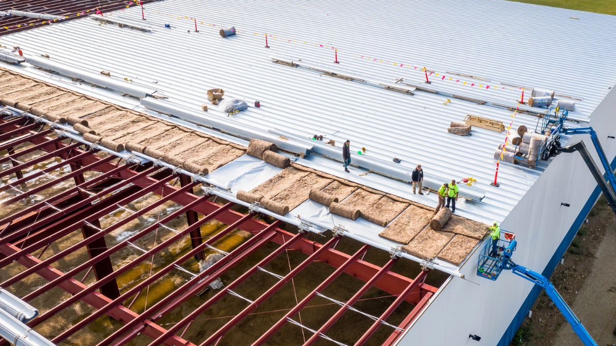 Workers installing quality insulation on metal structure roof improve energy efficiency, durability, and building performance.