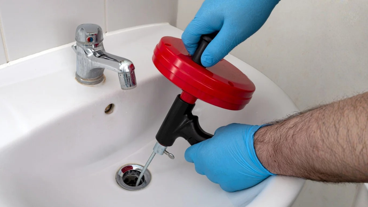 Plumber repairing rental property drain with hand snake