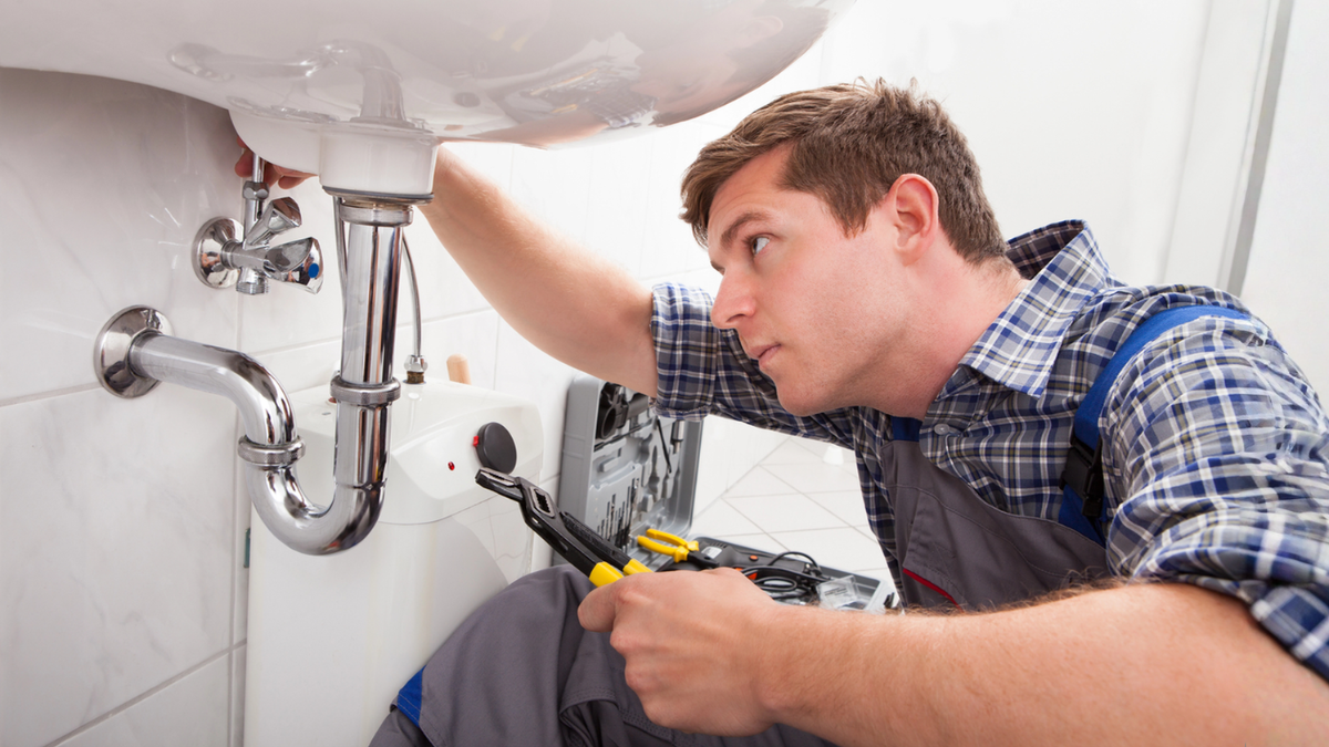 Plumber inspecting sink pipes during rental turnover checklist for landlords between tenant move-outs and inspections.