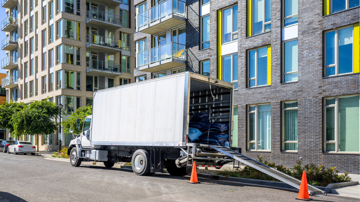 Moving truck outside apartment building shows long-distance moving costs and relocation expenses for 2026 renters.