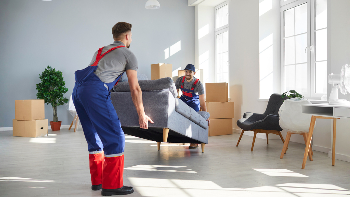 Long-distance movers carrying sofa into apartment showing mistakes to avoid when hiring relocation companies carefully.