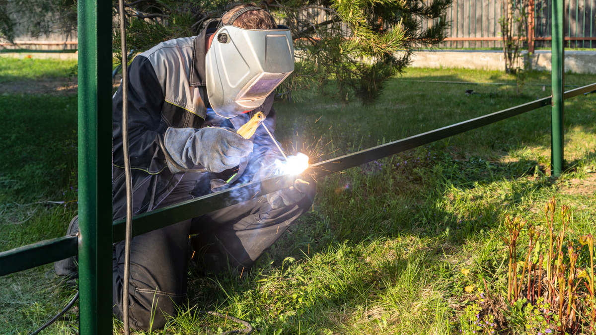 Welder performing property fence renovation with welding mask on.