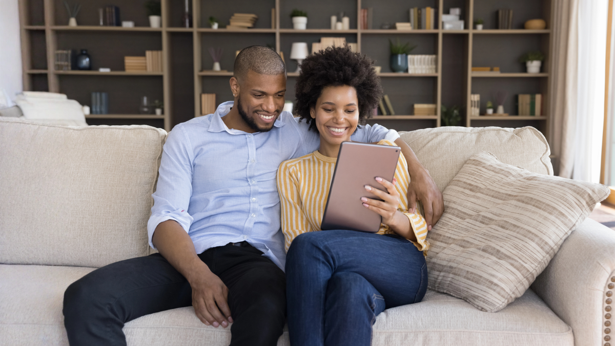 Homeowner couple sitting on couch researching how to sell their house without a perfect credit score.